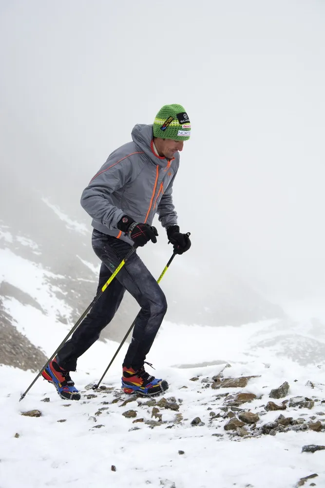 Mann mit Trekking Steigeisen und Stöcken im Schnee, Aufstieg in bergiger Landschaft.