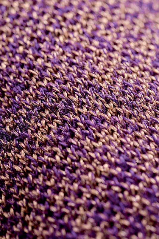 Nahaufnahme des Strickmusters einer Skisocke mit Merinowolle in Lila- und Beigetönen.