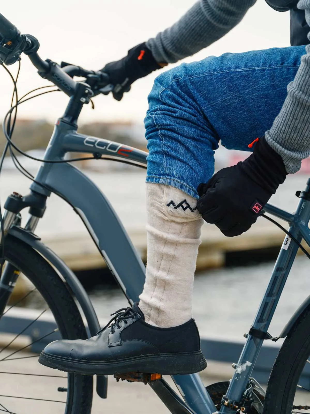 Persona con calzini e guanti riscaldati su una bicicletta. Il calzino è beige con un motivo a zig zag scuro.