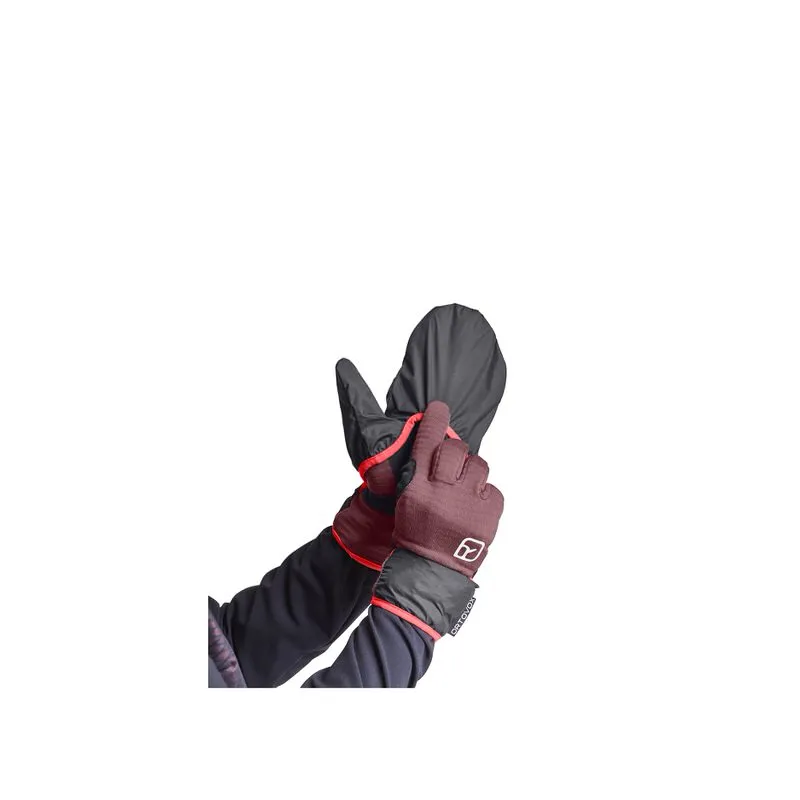 Le mani tirano il guanto Ortovox Fleece Grid Cover Glove W Mountain Rose sopra l'altro guanto.
