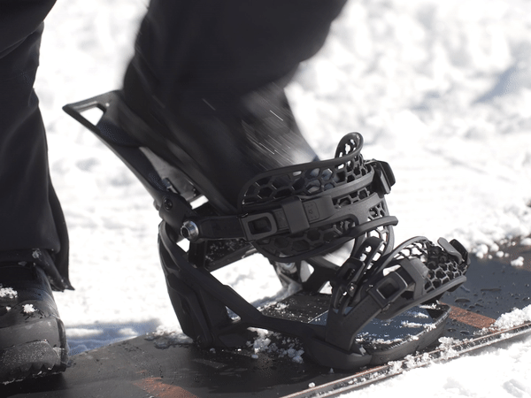 Schwarzer Snowboard-Schuh Ein schwarzer Snowboard-Schuh ist in eine schwarze Bindung auf einem Snowboard eingeschnallt.