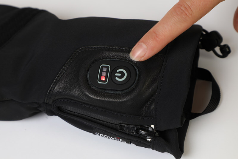Snowlife Heat DT Handschuh Nahaufnahme des Snowlife Heat DT Glove, Finger drückt den Power Knopf mit Batteriestatusanzeige.