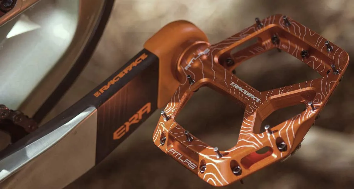 Nahaufnahme eines orangefarbenen Fahrradpedals mit weißen Höhenlinien und Stiften, montiert an einer ERA Kurbelgarnitur.