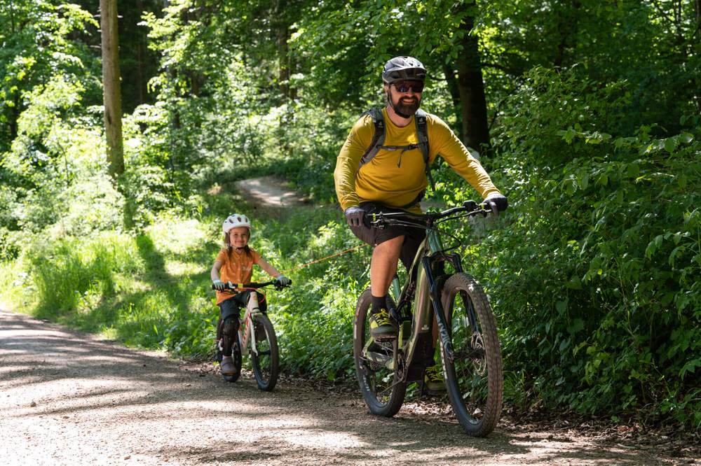 Father pulling child with the kommit pull system while cycling on a forest path.