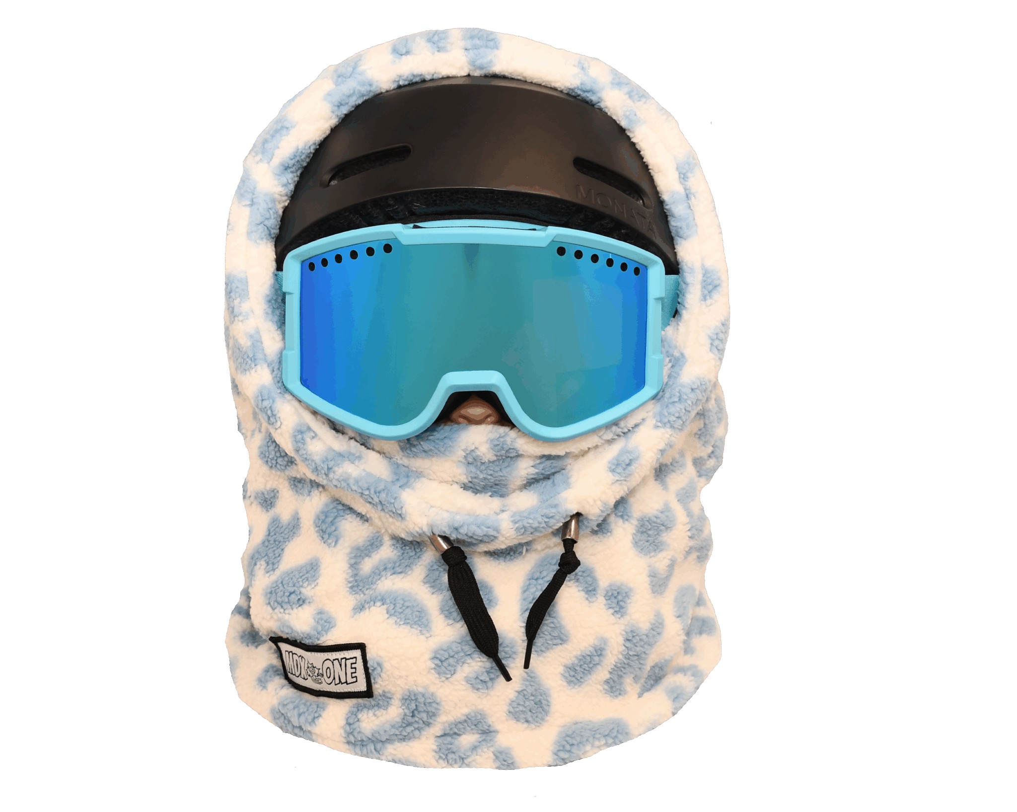 Cagoule moelleuse crème à taches de girafe bleues, portée sur un casque de ski noir. Lunettes de ski bleu clair à verres miroirs jusqu'au nez. Tissu doux protège tête et cou. Deux cordons noirs en bas.