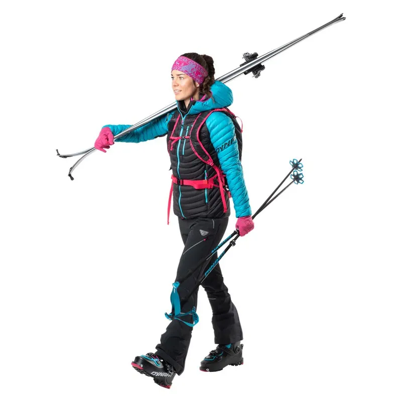 Femme en tenue de ski avec des skis et des bâtons. Elle porte une veste à capuche pour femme Dynafit Radical Down RDS de couleur Ocean.