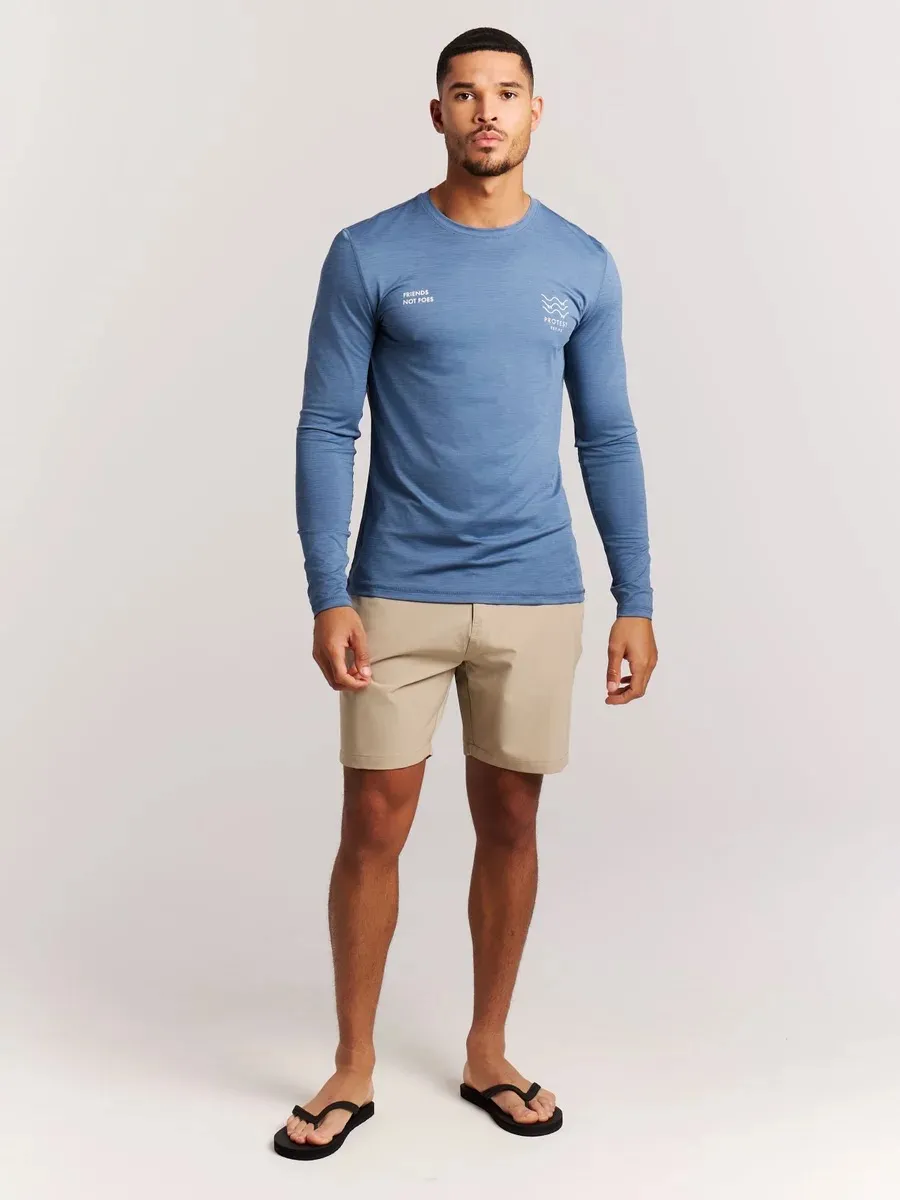 Man in blue long-sleeved shirt, beige shorts and toe separators against a white background.