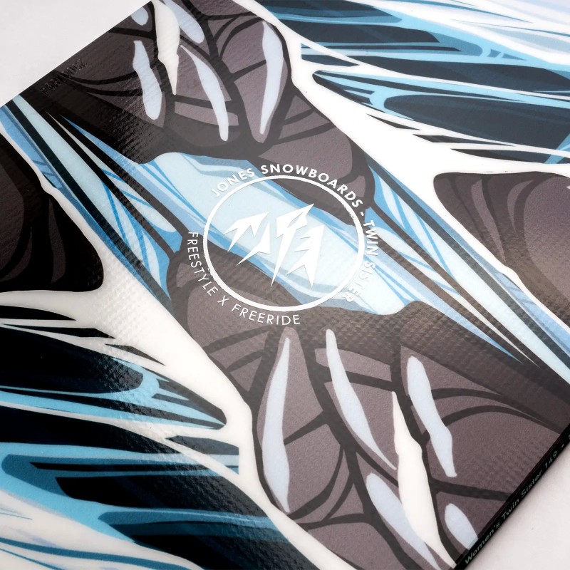 Jones Twin Sister Snowboard Detailaufnahme des Jones Twin Sister Snowboards mit abstrakten, blauen und grauen Grafiken und Herstellerlogo.