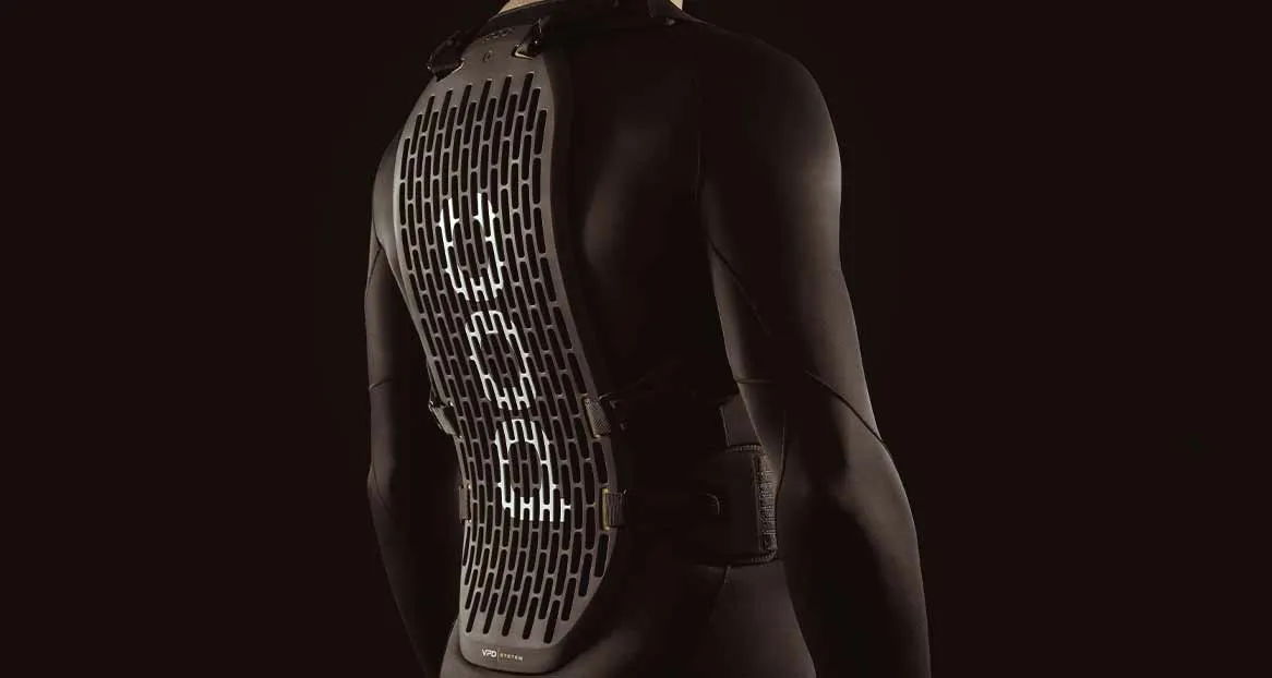 Black wetsuit with ventilated, gray back protector attached to the shoulders and waist. The background is dark and monochrome.