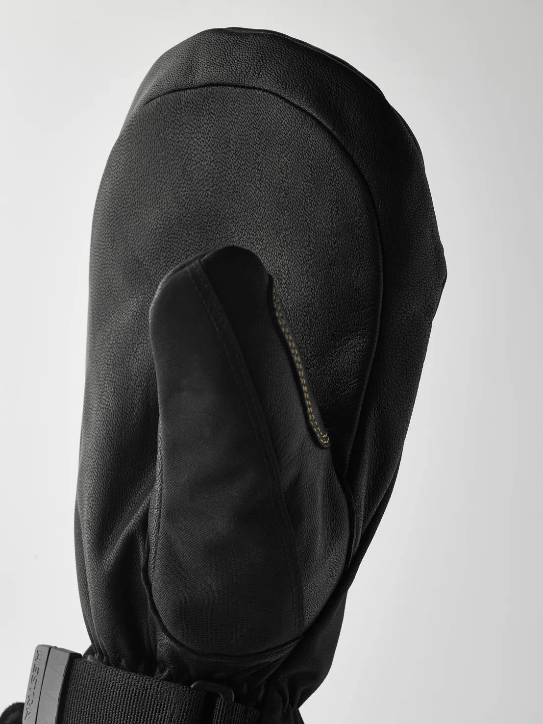 Close-up of a black leather glove with thumb, cuff with strap and buckle against a light background.