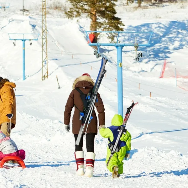 Winter scene: Family transporting skis with Skiback system on a snow-covered slope. Child wears blue skis.