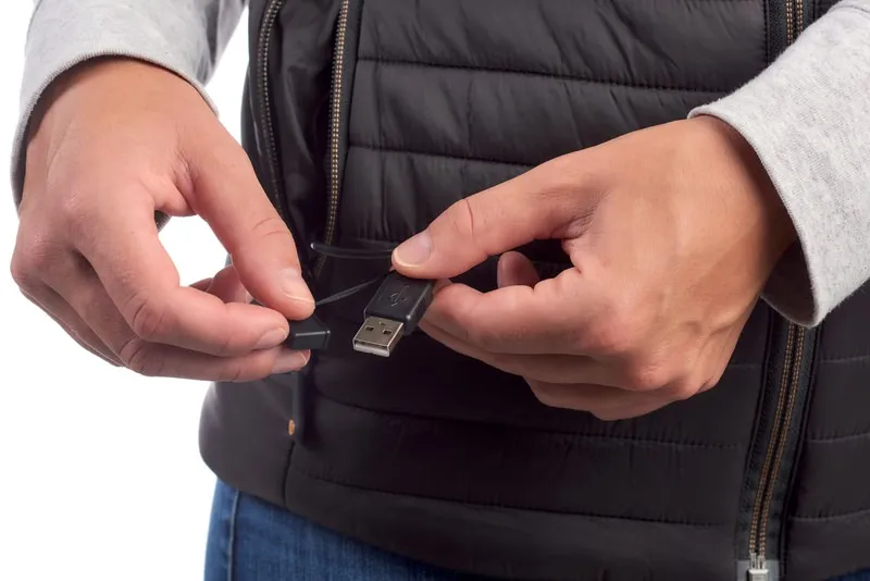 Nahaufnahme der Therm-ic Heated Vest mit USB-Kabel und Schutzkappe in Händen.