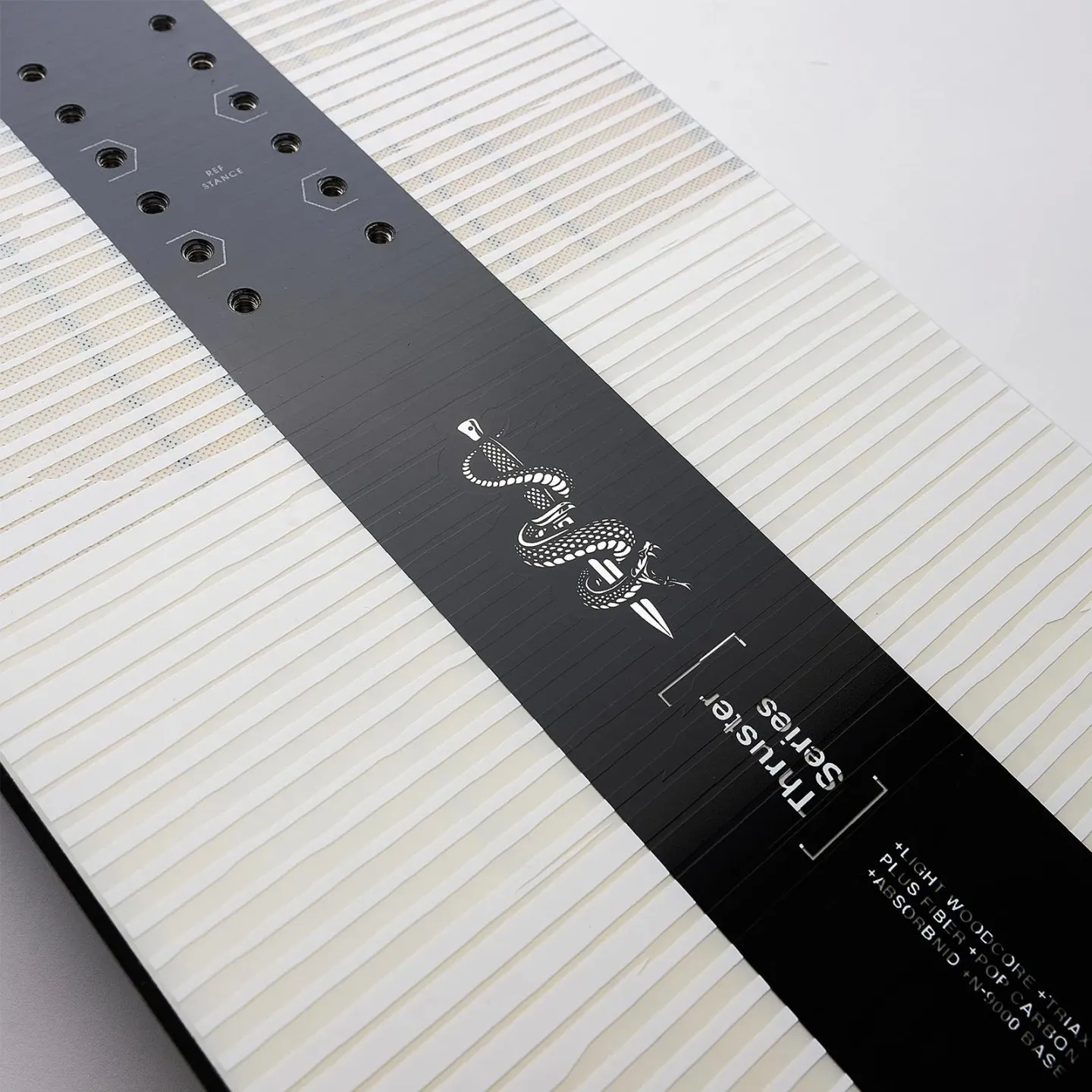 Vue détaillée Nidecker Thruster Snowboard : trous de fixation, graphisme de serpent sur planche à motifs noirs et blancs.
