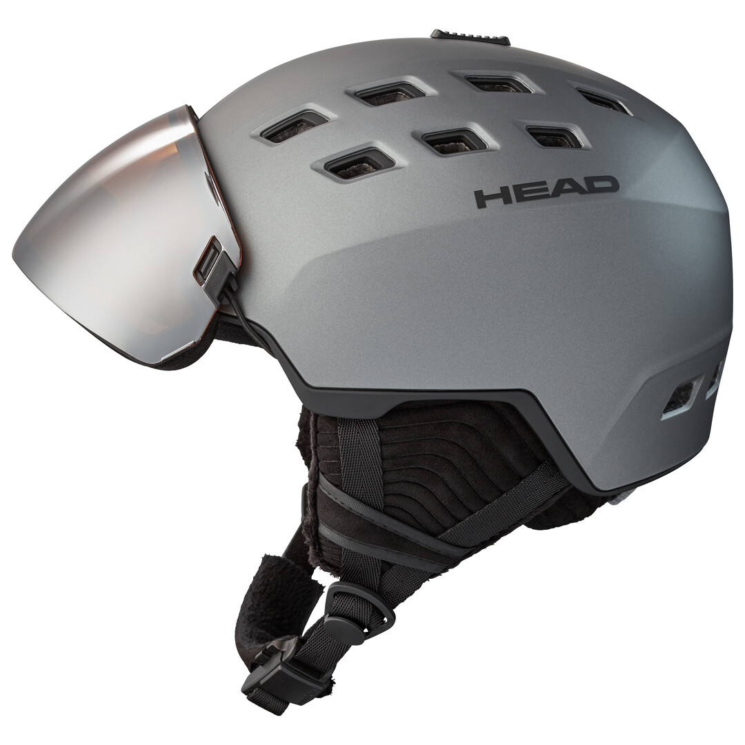 Grauer Skihelm mit Visier, mehreren Luftlöchern und Markenlogo "HEAD" seitlich. Kinngurt ist ebenfalls sichtbar.