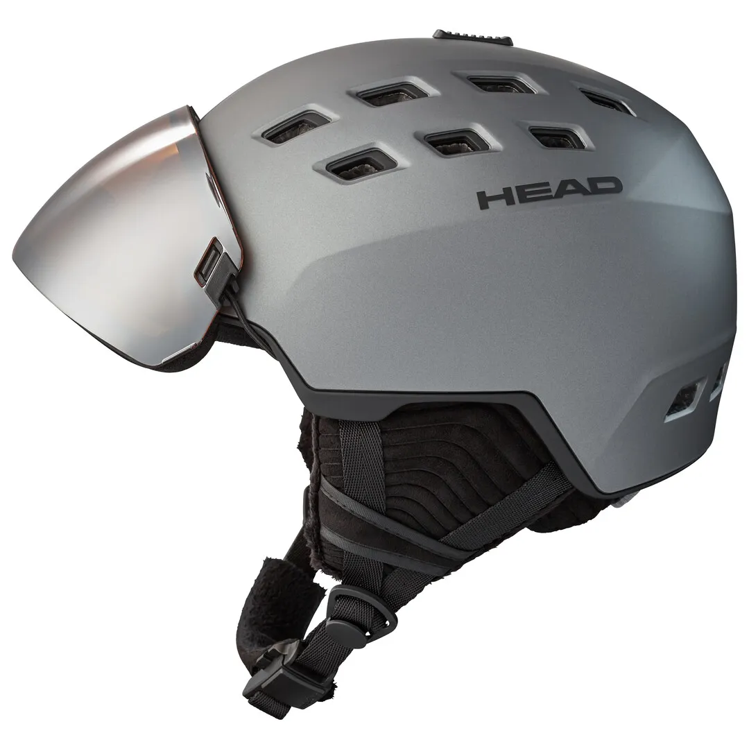 Grauer Skihelm mit Visier, mehreren Luftlöchern und Markenlogo "HEAD" seitlich. Kinngurt ist ebenfalls sichtbar.