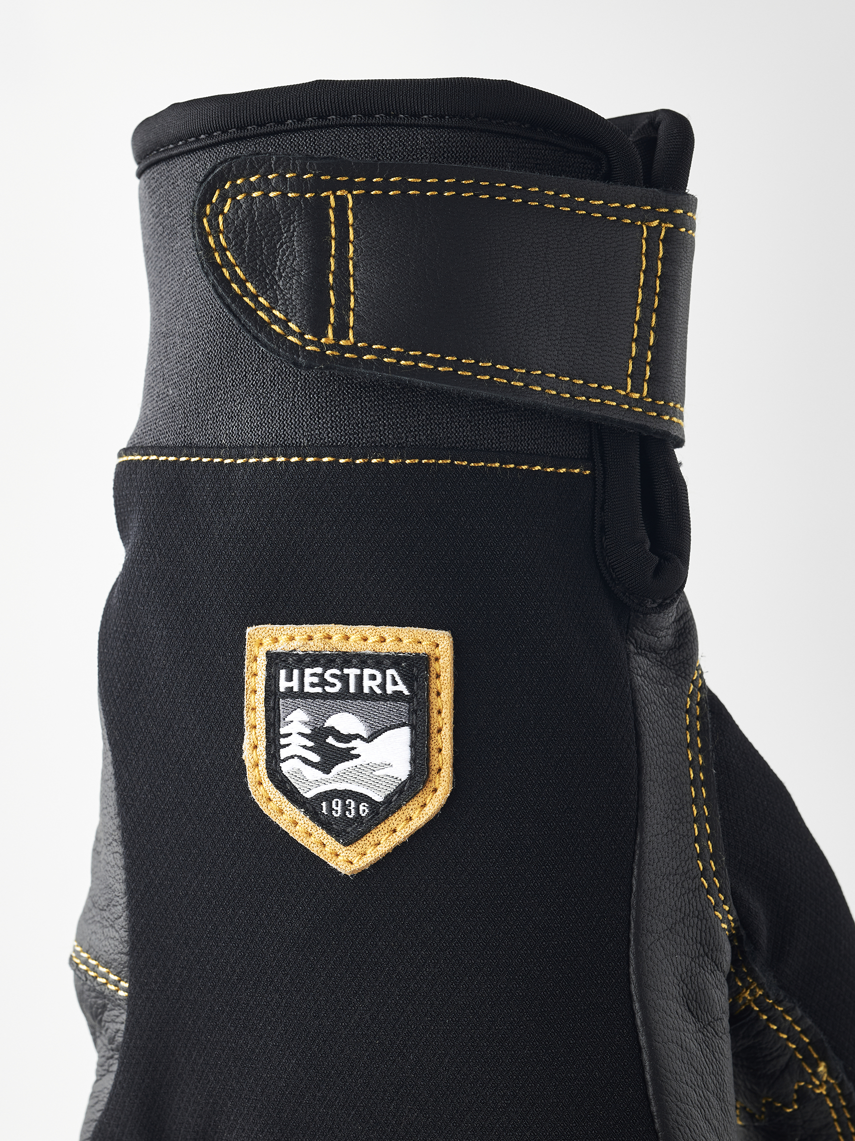 Détail d'un gant noir Hestra Ergo Grip Active avec coutures jaunes et logo de la marque.