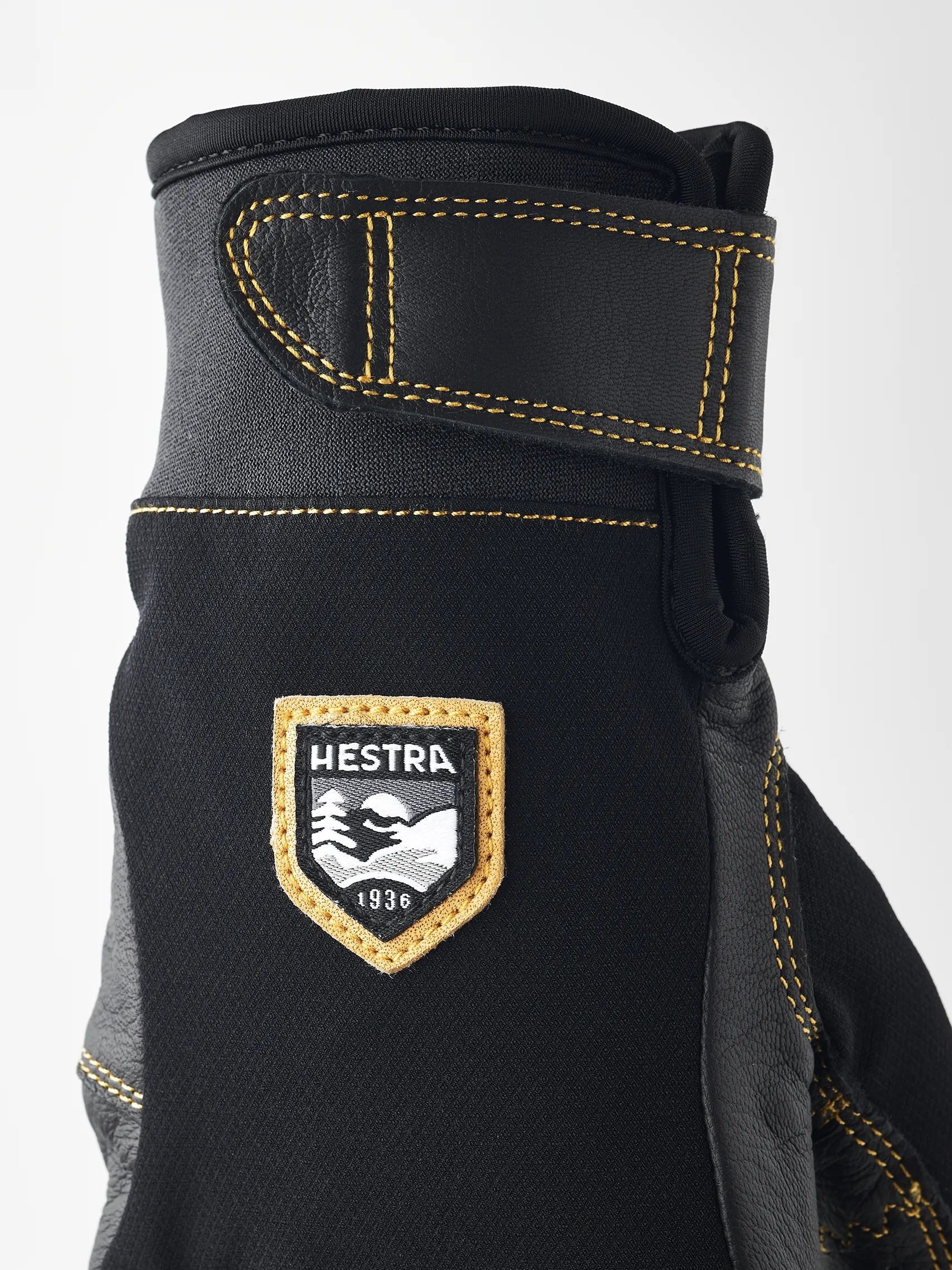 Detailaufnahme eines schwarzen Hestra Ergo Grip Active Handschuhs mit gelben Nähten und Markenlogo.