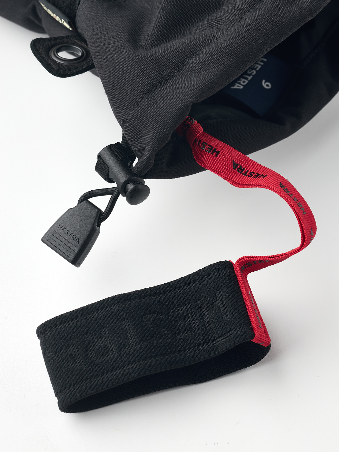 Black Hestra Gore-Tex gloves Close-up of a black Hestra Gore-Tex five-finger glove with red strap and black fastener.
