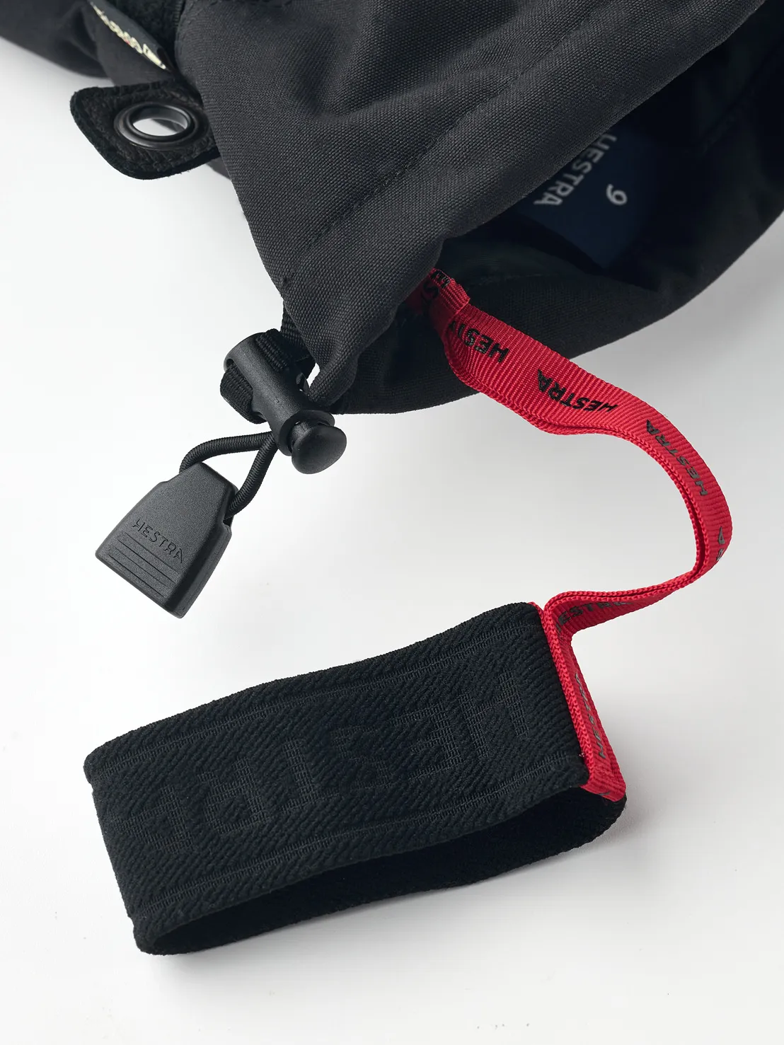 Vue détaillée d'un gant noir Hestra Gore-Tex à cinq doigts avec dragonne rouge et fermeture noire.