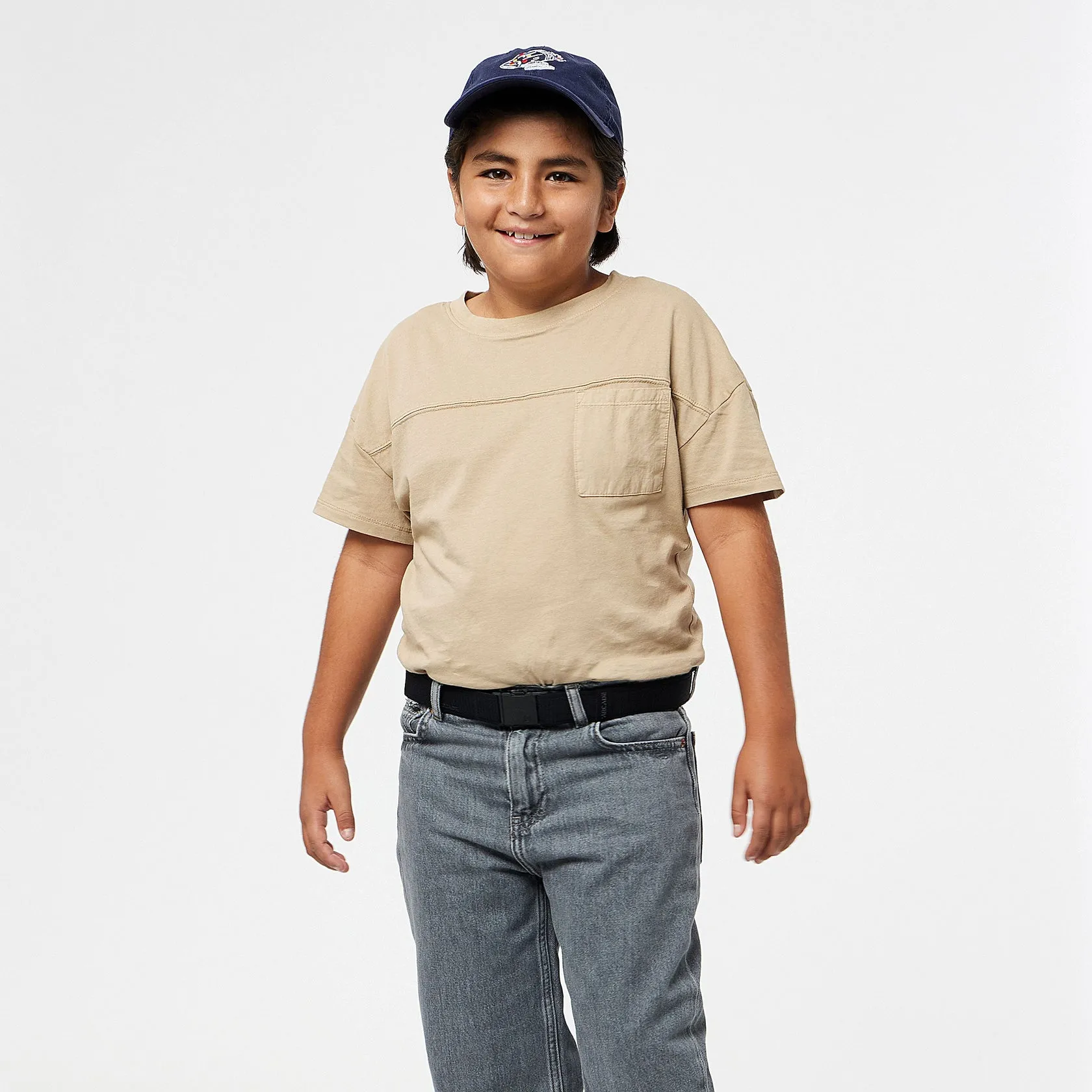 Kind mit blauem Basecap und beigem T-Shirt, trägt einen schwarzen Arcade Atlas Gürtel zu grauen Jeans.