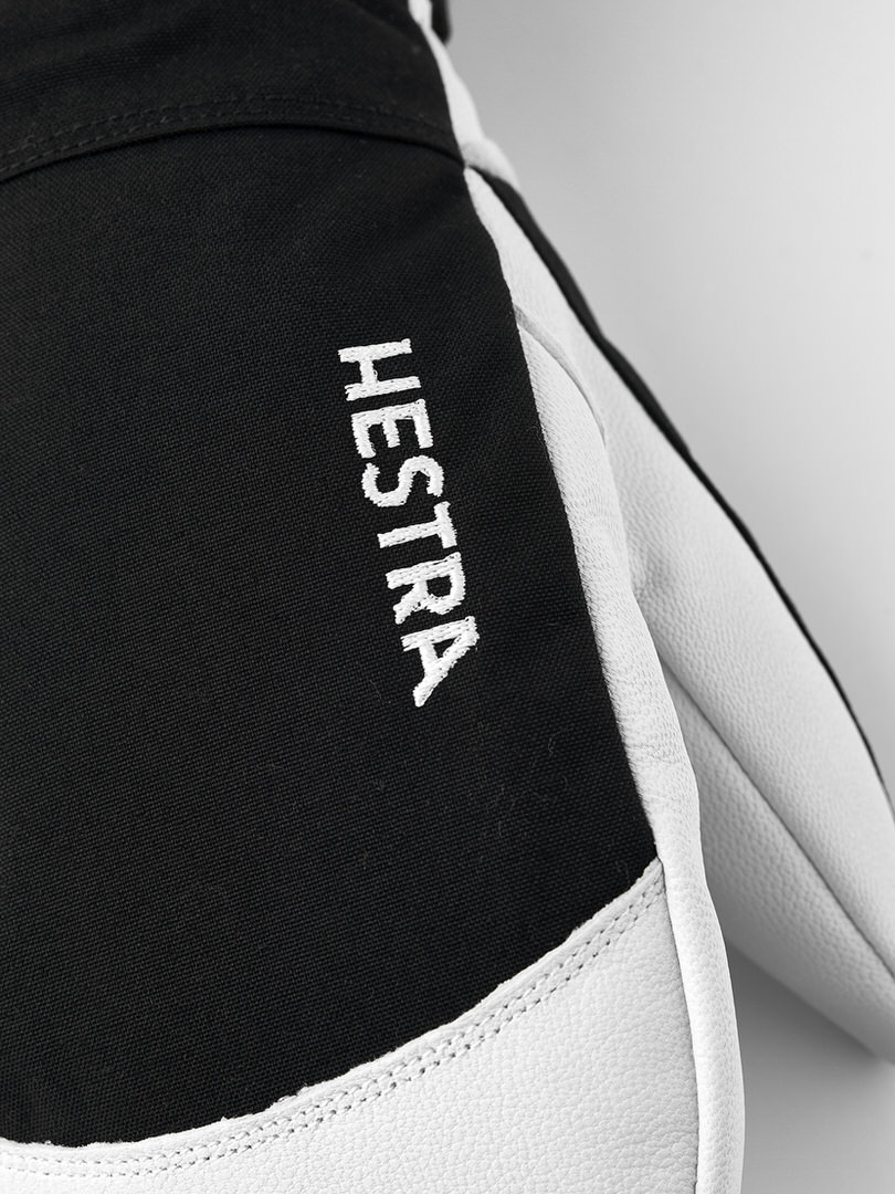 Nahaufnahme eines schwarzen Hestra-Handschuhs mit weißem Leder und dem weißen Schriftzug "HESTRA" auf der Oberseite.