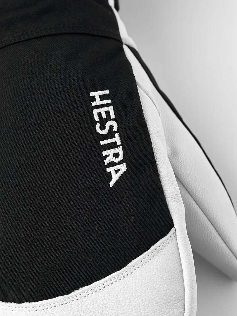 Gros plan sur un gant noir Hestra avec du cuir blanc et l'inscription blanche "HESTRA" sur le dessus.
