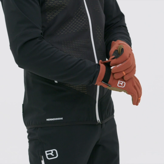 Person zieht Rock'n'Wool Glove Liner in Rotbraun an, trägt schwarze Sportkleidung.