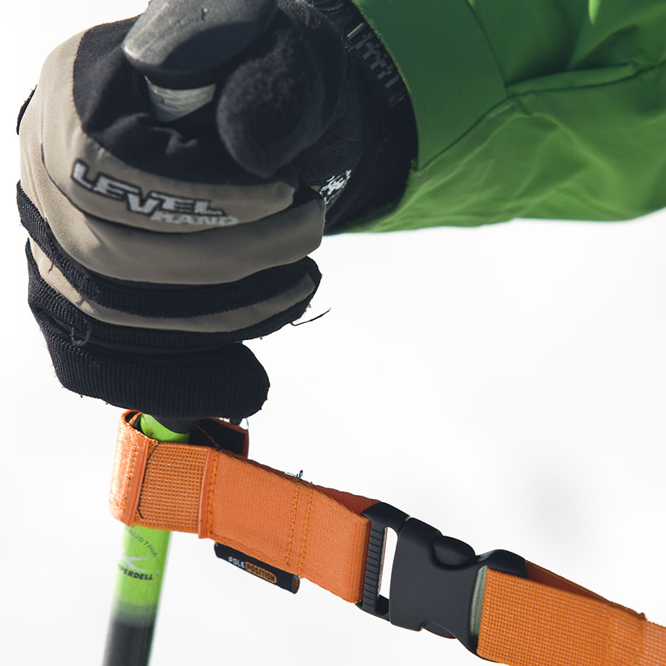 Nahaufnahme Hand mit Handschuh am Griff eines Skistocks mit orangem Training Strap.