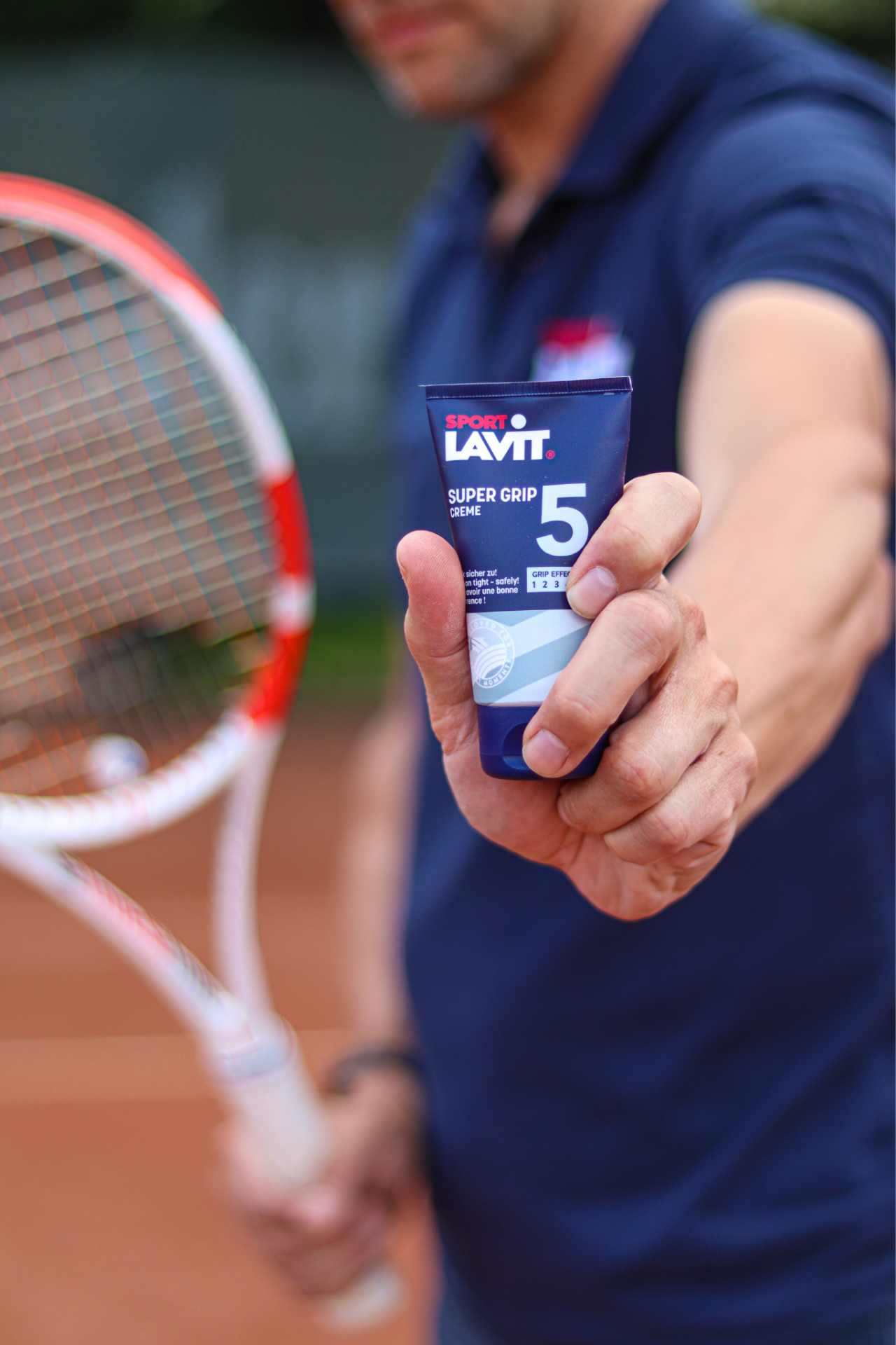 Mann hält SPORT LAVIT Super Grip Creme mit Tennisschläger im Hintergrund.