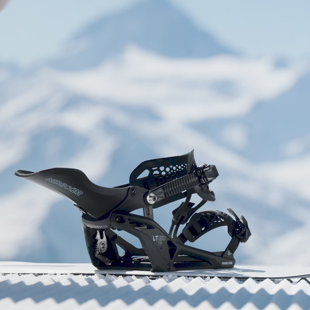 Fixation de snowboard noire de Nidecker sur un snowboard, avec des montagnes enneigées en arrière-plan. Les détails tels que les sangles et les boucles sont reconnaissables.