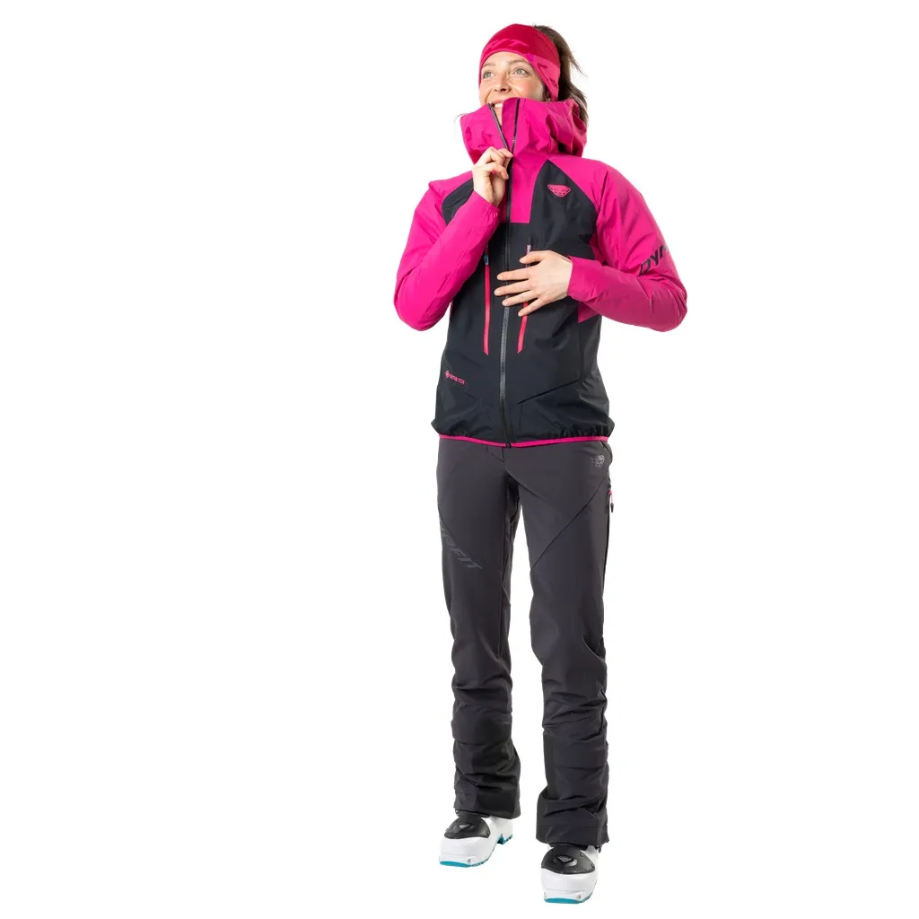 Donna in pantaloni Dynafit TLT Touring DST, neri, giacca rosa, scarponi da sci, con lo sguardo rivolto verso l'alto.