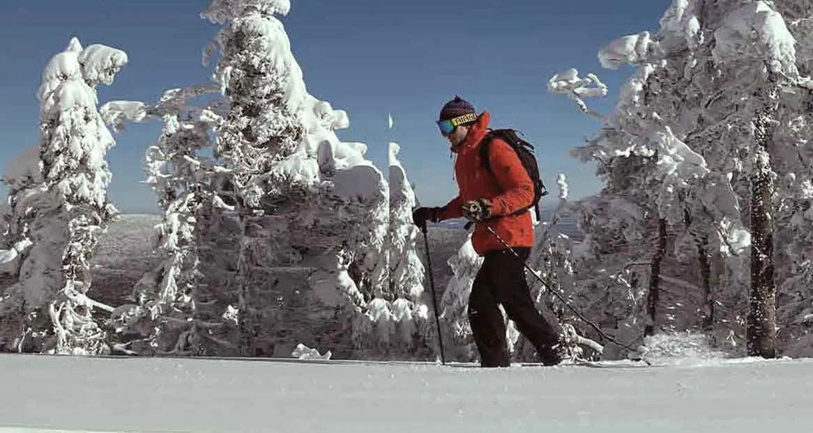 Person with red jacket and ski goggles snowshoeing in a snowy winter landscape.