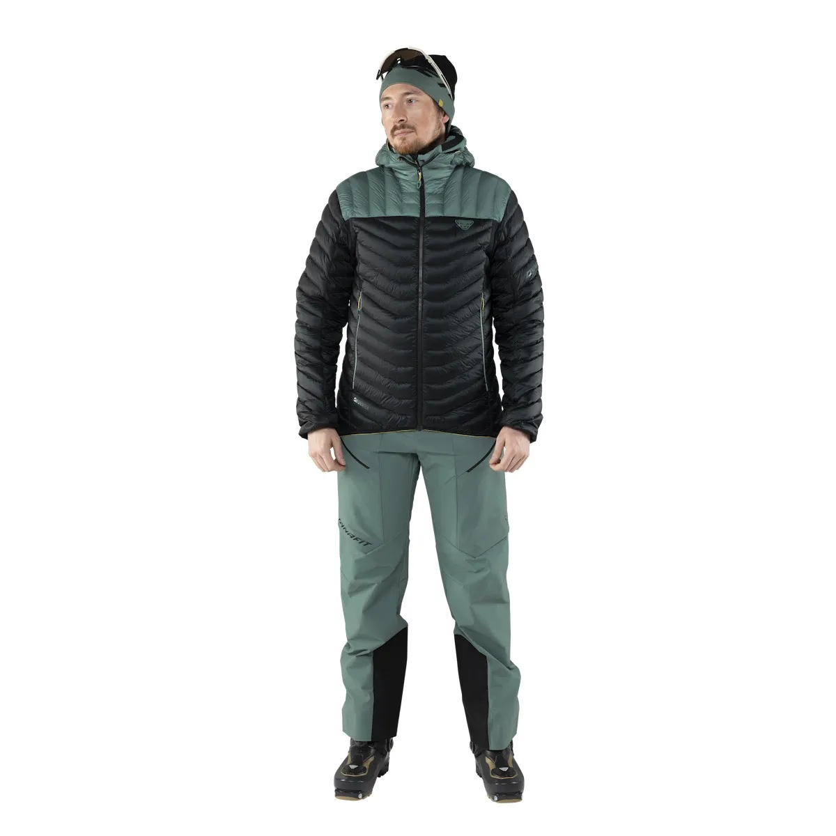 Uomo in piumino e pantaloni da sci alpinismo, su sfondo bianco. La giacca è nera e verde.