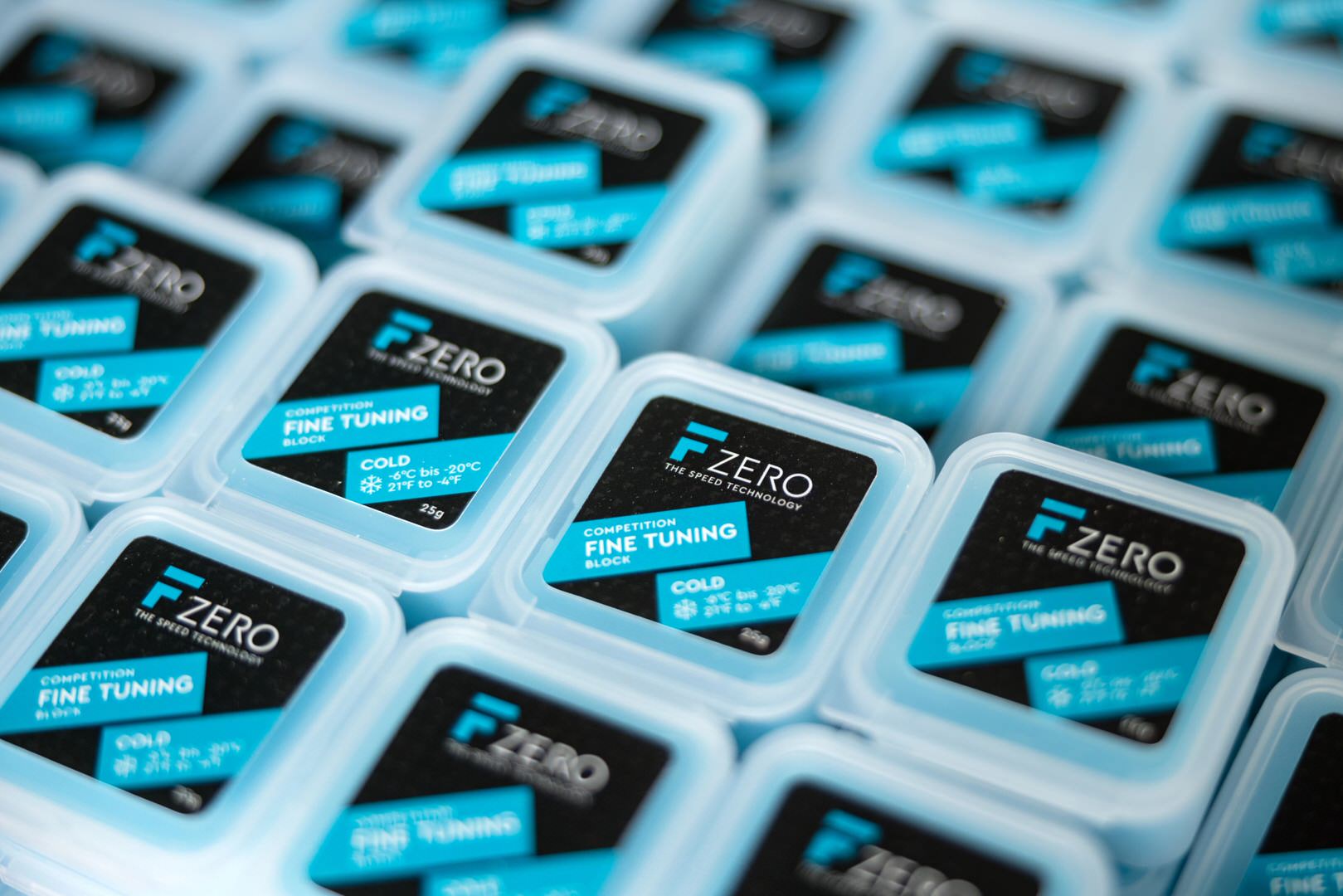 De nombreux récipients carrés bleus avec des étiquettes noires aux accents bleus et l'inscription "FZERO FINE TUNING " sont disposés les uns près des autres.