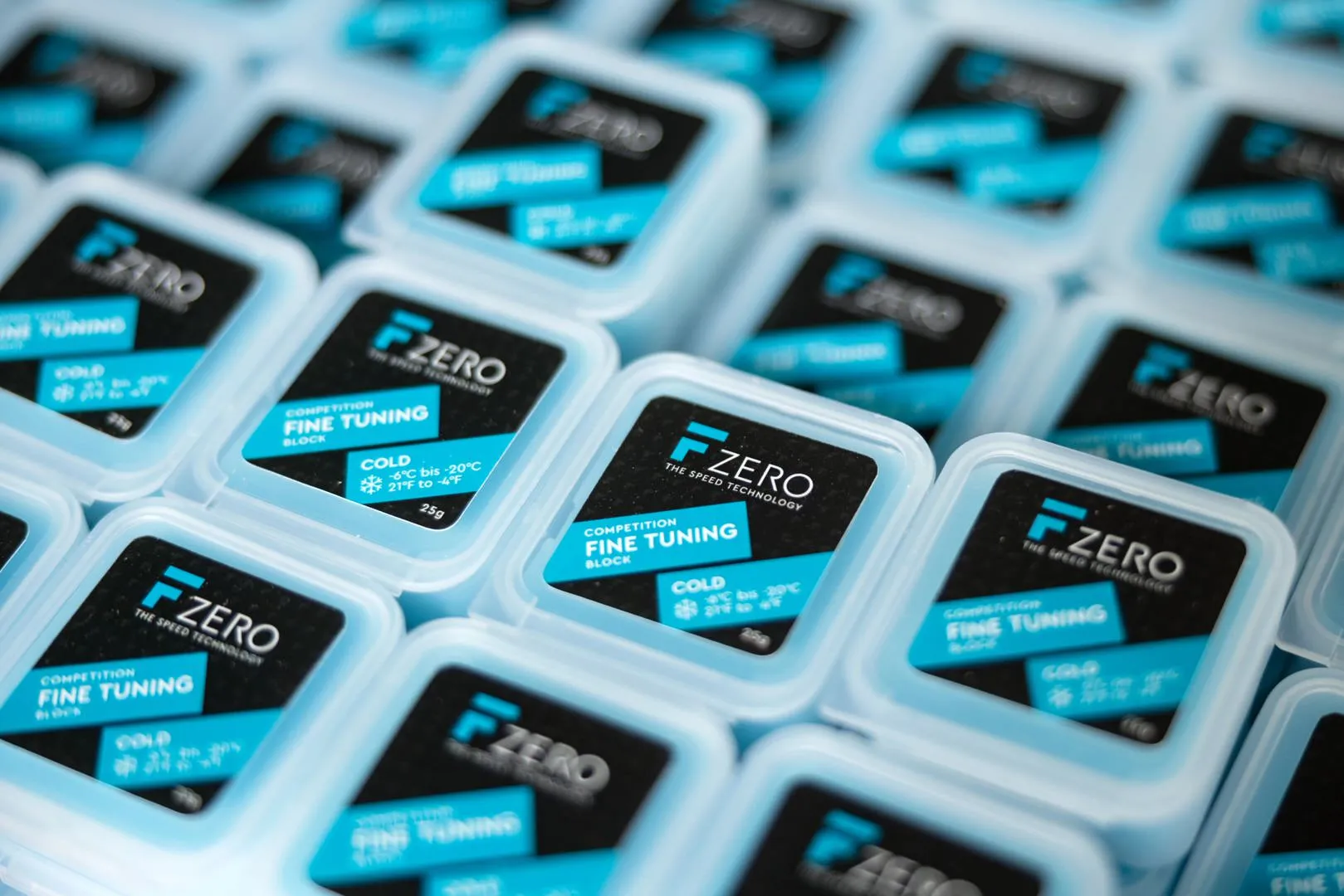 Viele blaue, quadratische Behälter mit schwarzen Etiketten mit blauen Akzenten und der Aufschrift "FZERO FINE TUNING" liegen dicht aneinander.