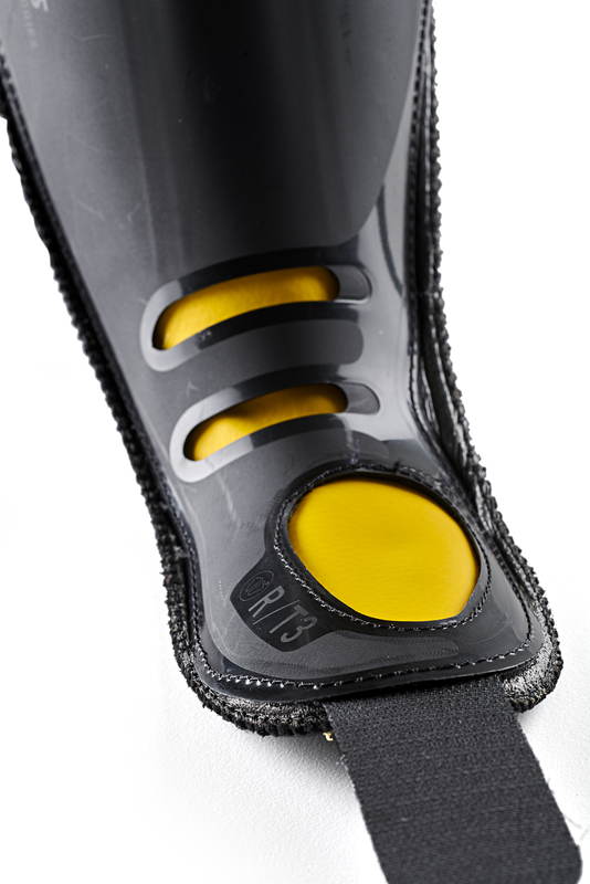 Primo piano di un parastinchi nero con imbottitura gialla e cinturino nero.