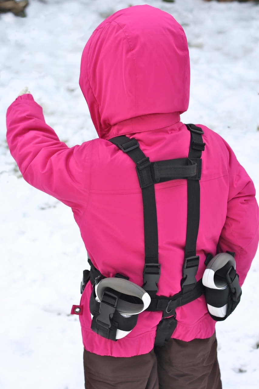 Enfant dans la neige avec une veste rose et une aide au ski Lil' Ripper Gripper dans le dos.
