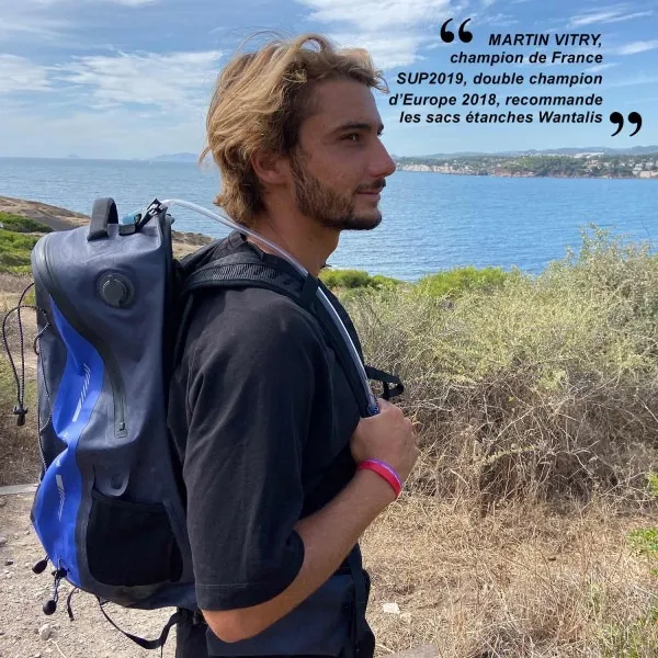 Homme avec un sac à dos étanche de 35L avec système d'hydratation devant un paysage côtier. Citation de Martin Vitry en arrière-plan.