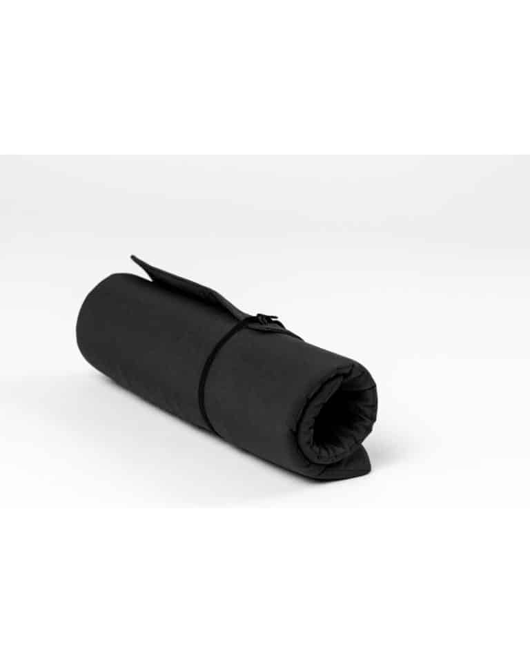 Eine zusammengerollte, schwarze Matte, fixiert mit einem Band, liegt auf einem weißen Untergrund.