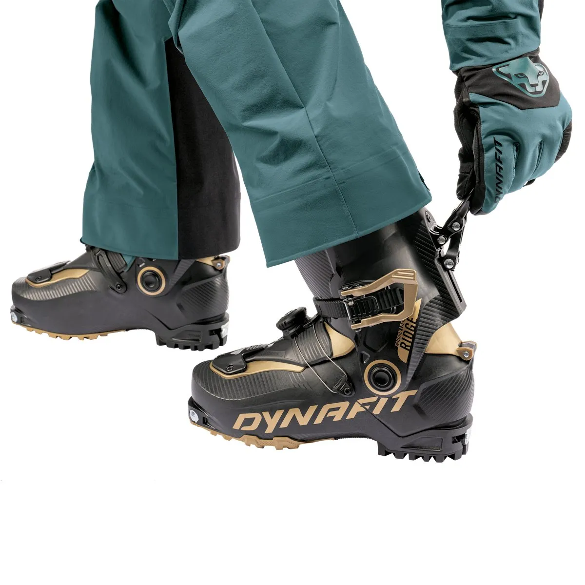 Close-up: Person closes Dynafit ski touring boot with matching gloves and green ski trousers.