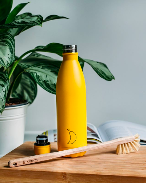 Yellow Chillys bottle, lid and brush on wooden board. Plant in the background.