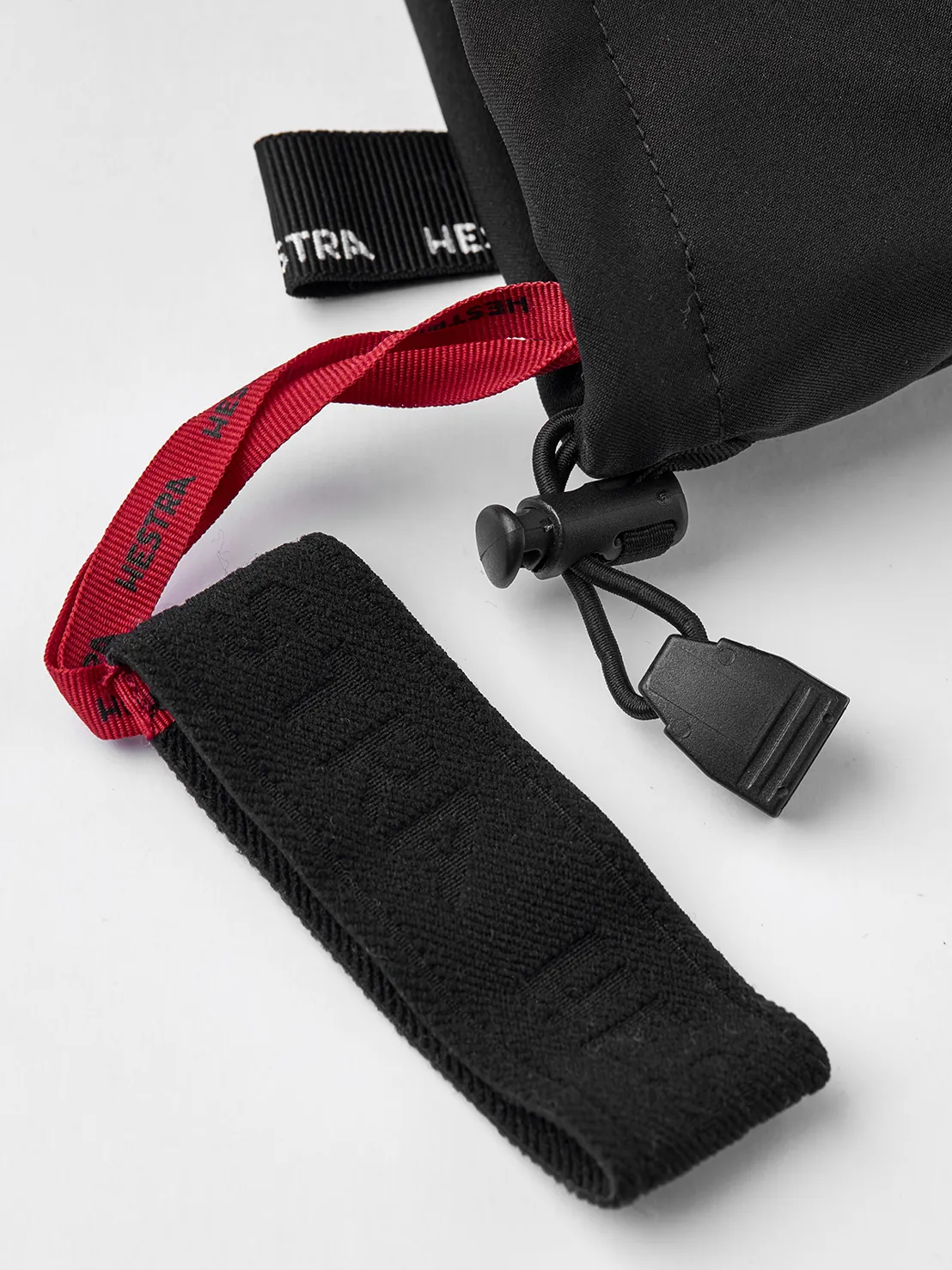 Vue détaillée d'un gant noir Hestra Army Leather Extreme Mitt, avec cordon de serrage et dragonne rouge.