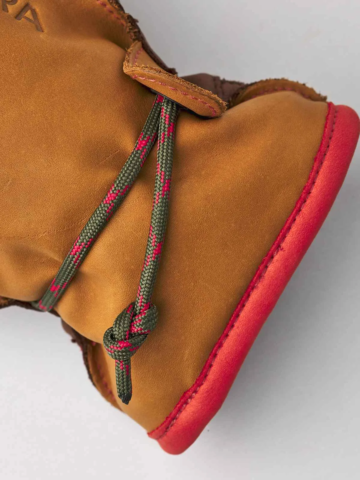 Nahaufnahme des Hestra Wakayama Handschuhs mit grün-roter Schnur, Leder, rotem Saum und Paracord-Schließe.