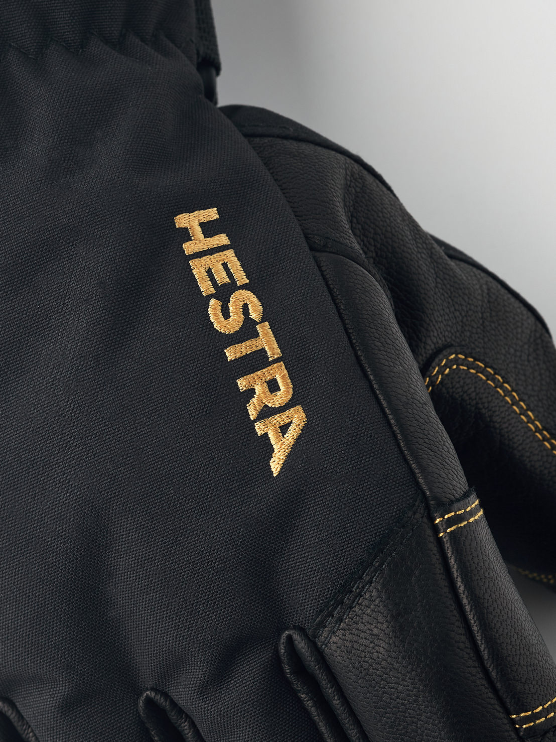 Black Hestra gloves Close-up of a black Hestra Gore-Tex five-finger glove with gold-colored Hestra logo.