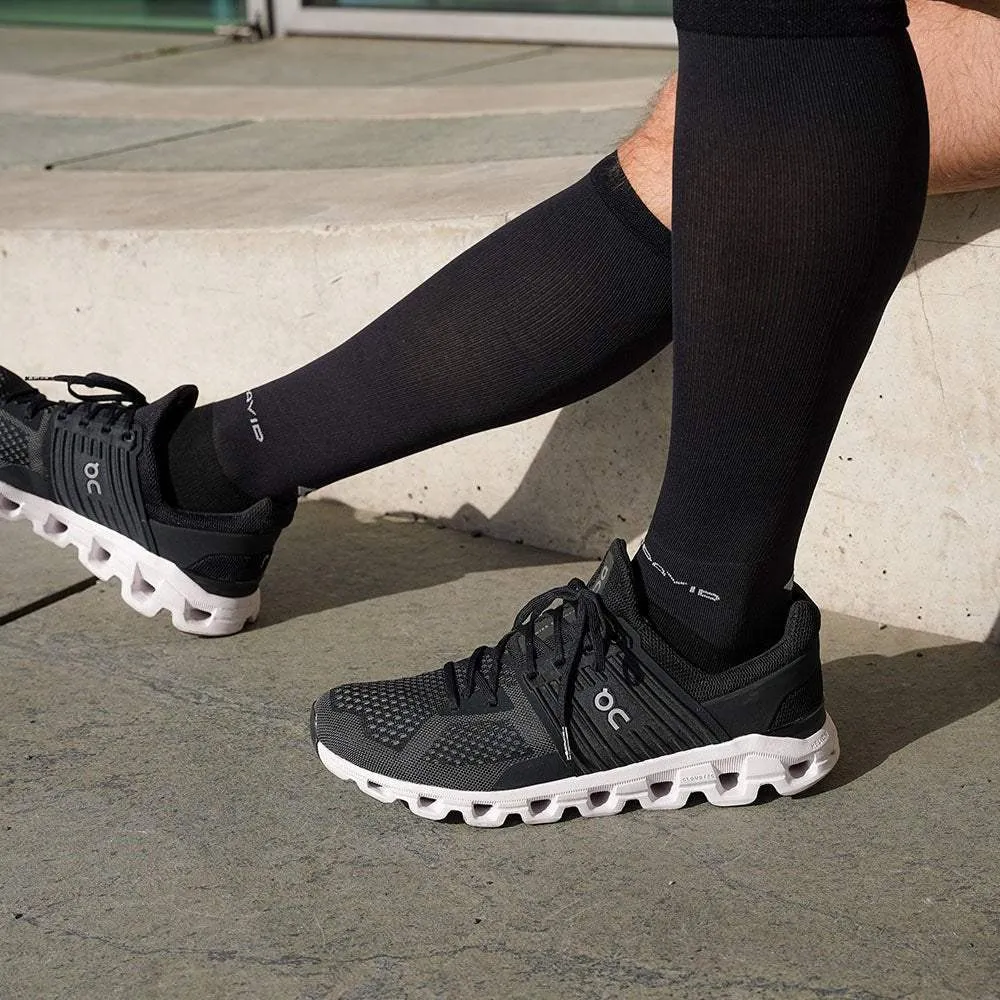 Legs with black MCDavid compression socks and sneakers on a stone staircase.