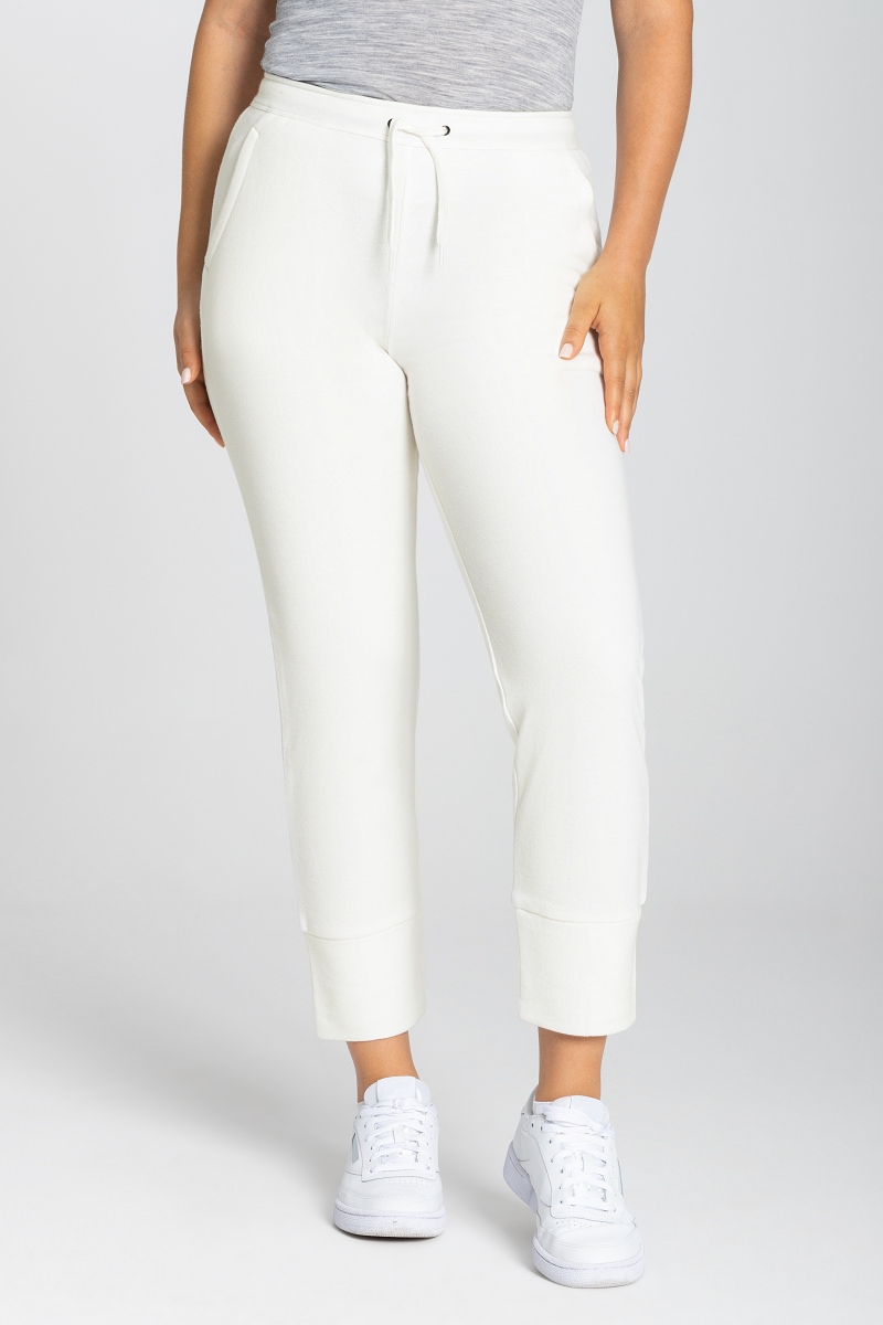 Eine Person trägt eine Super.Natural W Knit Pant in Fresh White, kombiniert mit weißen Sneakers.
