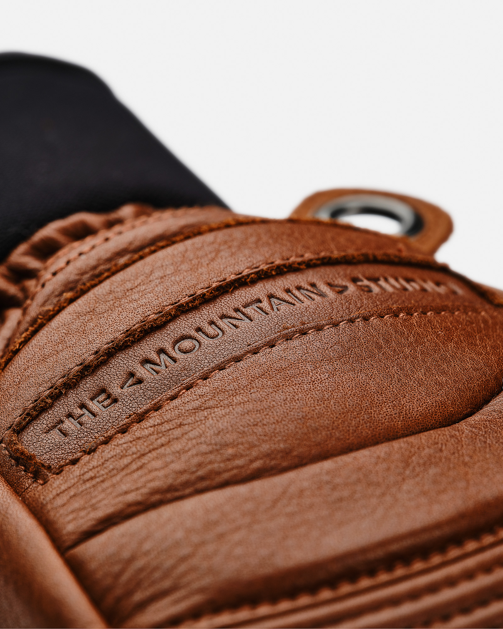 Detailaufnahme brauner Lederhandschuh mit Logo "THE MOUNTAIN STUDIO", Nähte und Öse sichtbar.