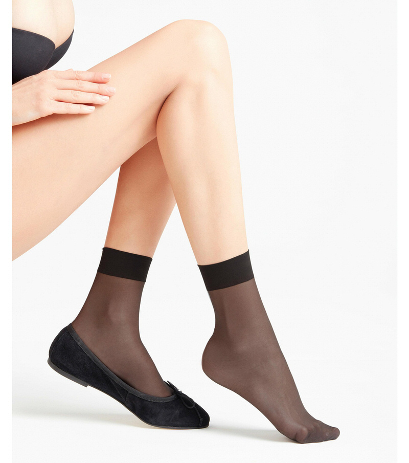 Jambes avec des chaussettes noires transparentes de 15 DEN et des ballerines sur fond blanc.