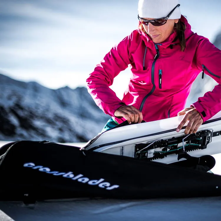 Woman packs Crossblades in a black bag with logo in front of a snow-covered mountain backdrop.