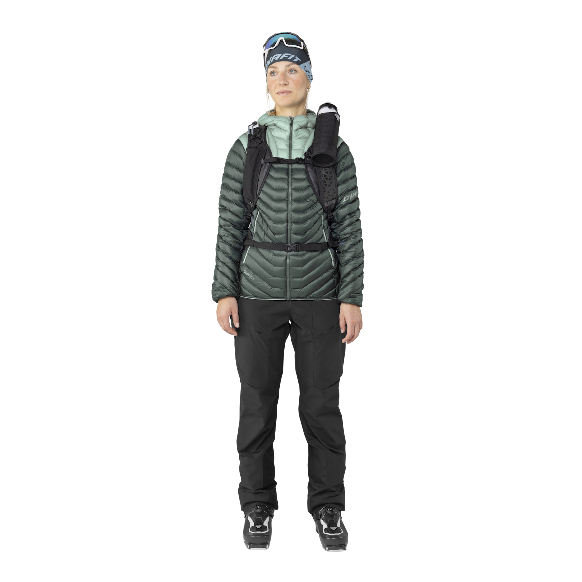 Vêtements de ski dynamiques Une femme en tenue de ski, avec Dynafit Ridge Ultralight doudoune verte, pantalon et chaussures de ski.